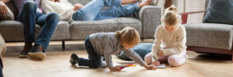 Little kids playing on floor of living room with parents resting on couch
